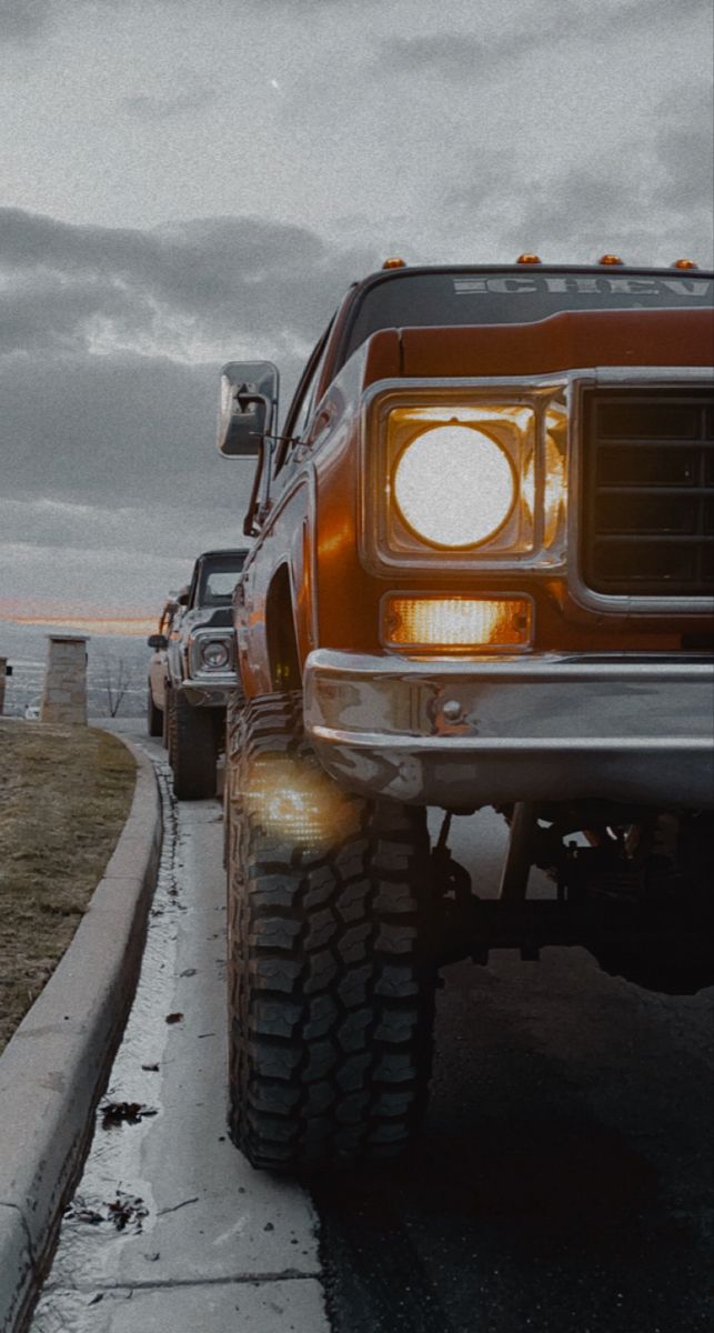 two trucks are parked on the side of the road with their lights turned on and one is off