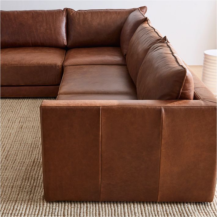 a large brown leather couch sitting on top of a carpeted floor next to a white vase