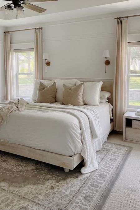 a large white bed sitting inside of a bedroom next to two windows and a ceiling fan