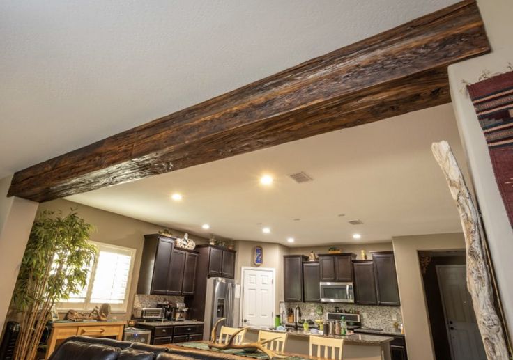 a living room and kitchen area with wood beams on the ceiling, black leather couches