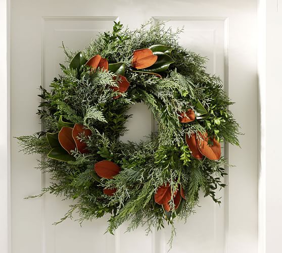 a wreath is hanging on the front door with oranges and greenery around it