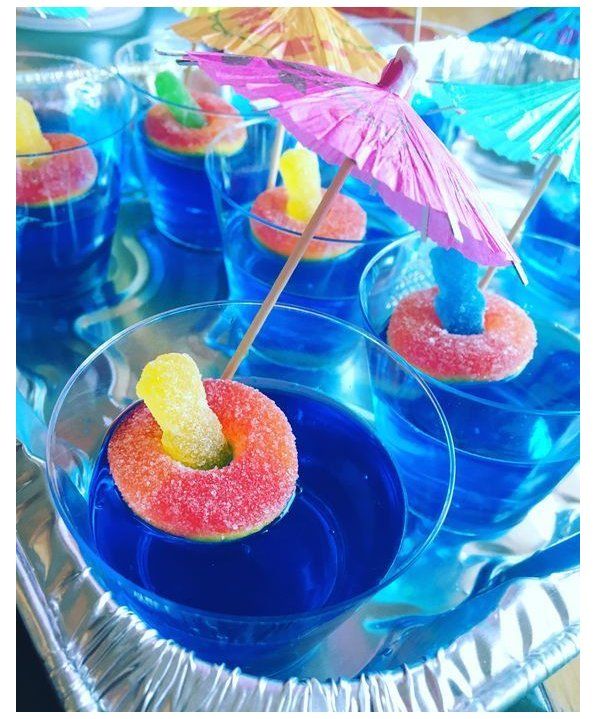 small desserts are arranged in clear bowls with umbrellas on the top and blue water