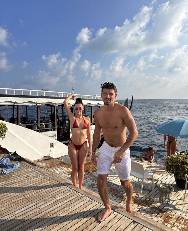 a man and woman standing on a dock next to the ocean