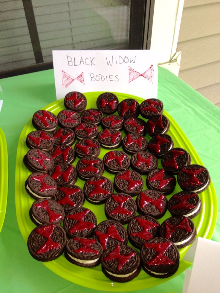 a green plate topped with lots of cookies covered in red icing next to a sign that says black widow bodies