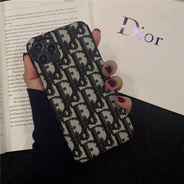 a woman is holding up her phone case in front of an open book, which has a pattern on it