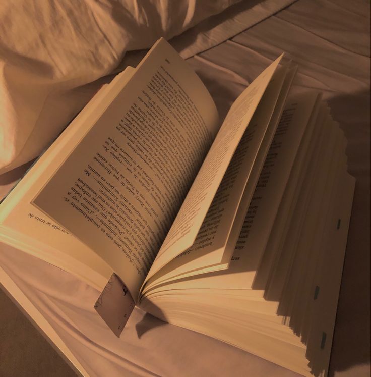 an open book sitting on top of a bed next to pillows and sheets with the pages folded down