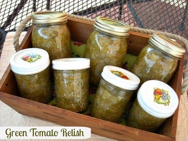 four jars filled with green tomato relish sit in a wooden box on a table