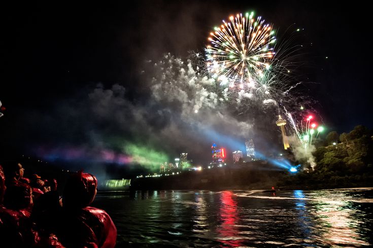 fireworks are lit up in the night sky and reflecting on the water as people watch