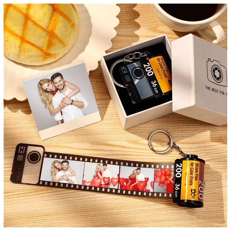 a camera keychain sitting on top of a wooden table next to a cup of coffee