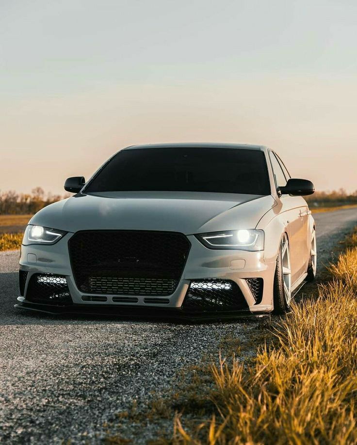 a white car parked on the side of a road next to tall grass and bushes