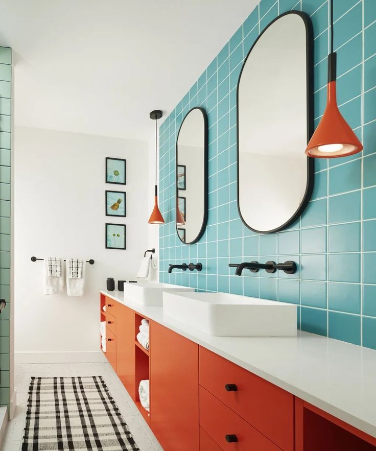 a bathroom with blue and orange tiles on the walls, two mirrors above the sinks