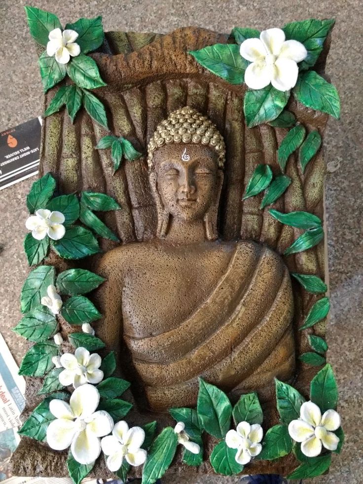 a buddha statue sitting on top of a table next to white flowers and green leaves