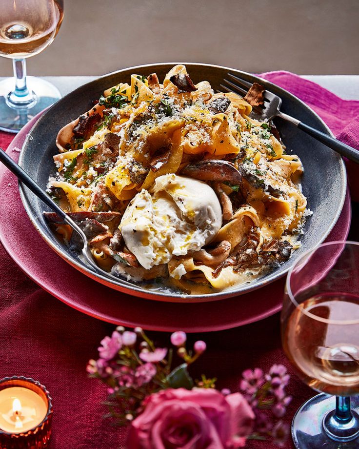 a plate of pasta with meat, cheese and sauce on a table next to two wine glasses