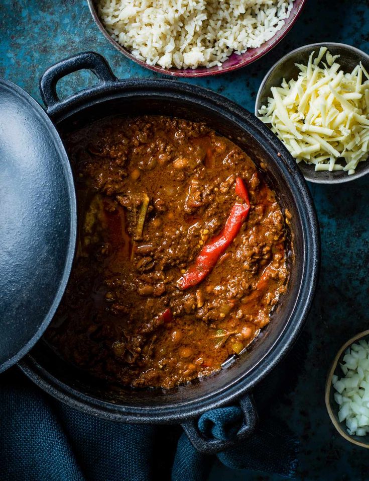 two bowls filled with chili and cheese next to other food on a blue tablecloth