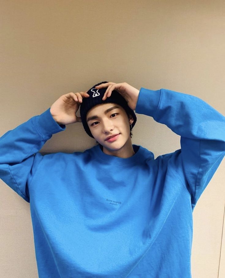 a young man is wearing a blue sweatshirt and black hat with his hands on his head