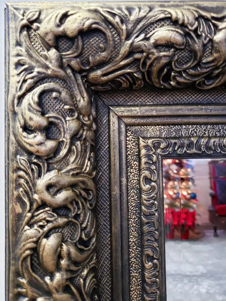 an ornate gold frame with a mirror in the middle and a christmas tree behind it