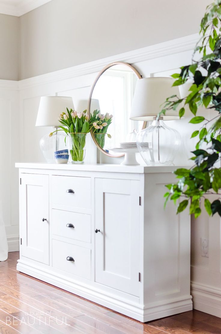 a white dresser with plants and lamps on top