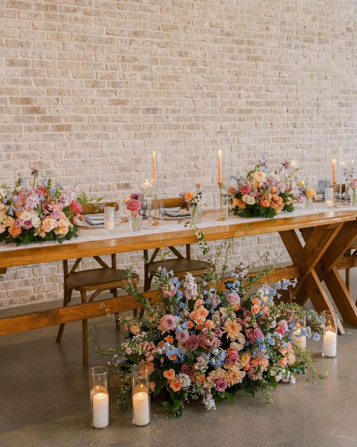 a long table with flowers and candles on it in front of a white brick wall