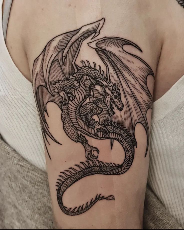 a woman's arm with a dragon tattoo on the back of her shoulder,