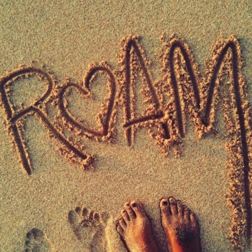 the word roma written in sand with two people's feet and one person's legs