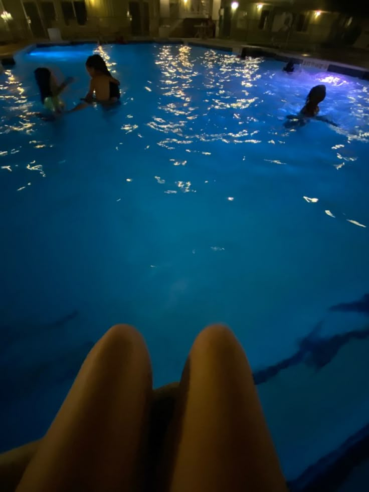 people are swimming in the pool at night with their feet propped up on the edge