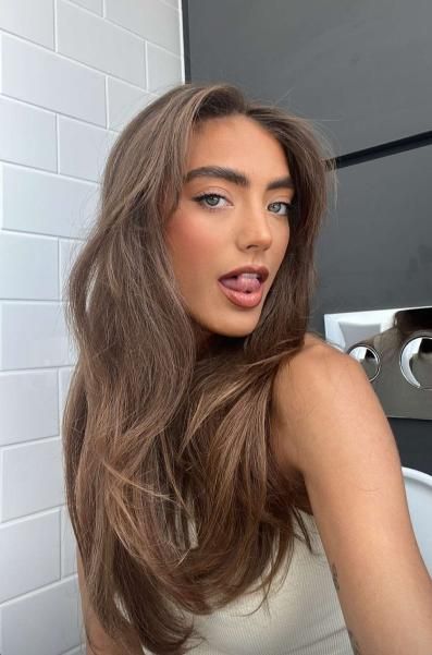 a woman with long hair standing in front of a white brick wall and posing for the camera