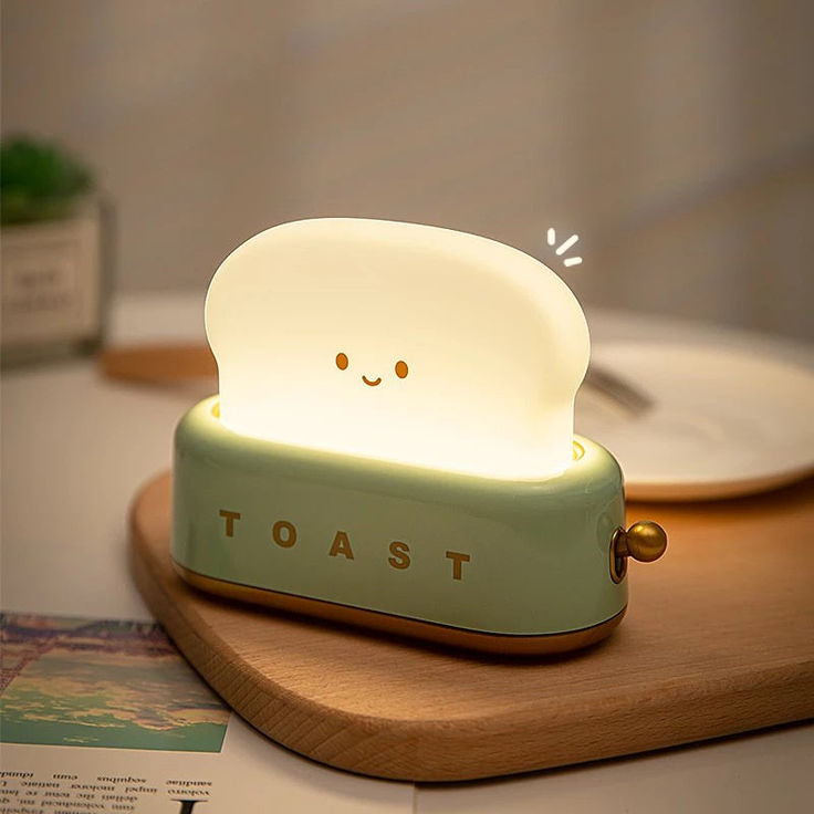 a cute little toaster shaped lamp on top of a wooden table next to a plate