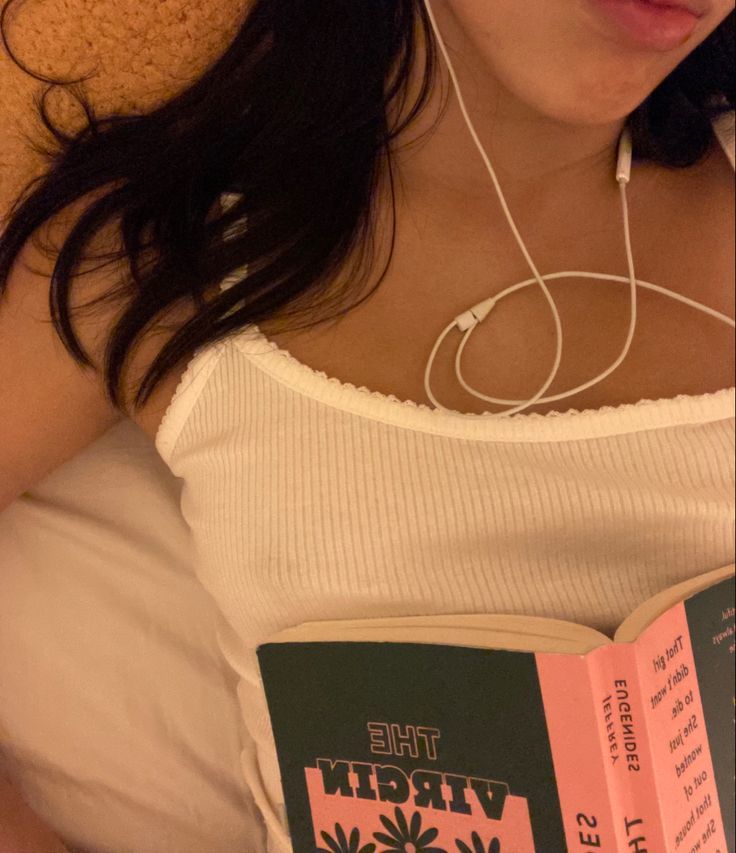 a woman laying in bed reading a book with headphones attached to her earbuds