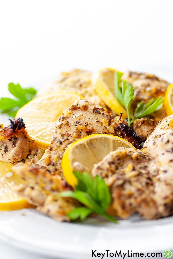 a white plate topped with chicken covered in lemons and garnished with herbs