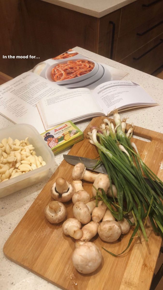 mushrooms and onions are on a cutting board next to an open cookbook with the recipe book in the background