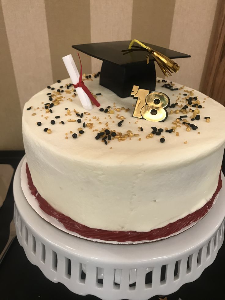 a white cake with black and gold sprinkles on it, topped with a graduation cap