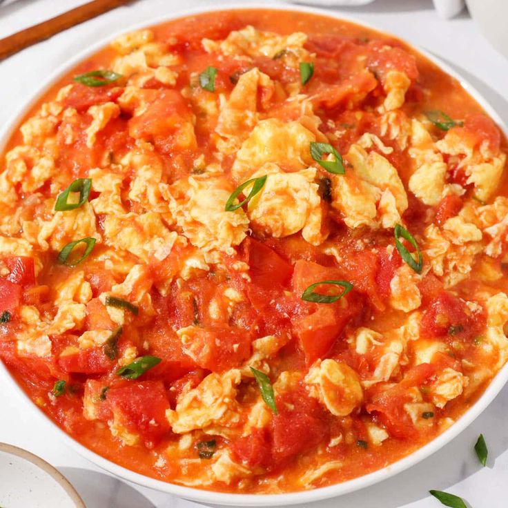 a white bowl filled with eggs, tomatoes and other food on top of a table