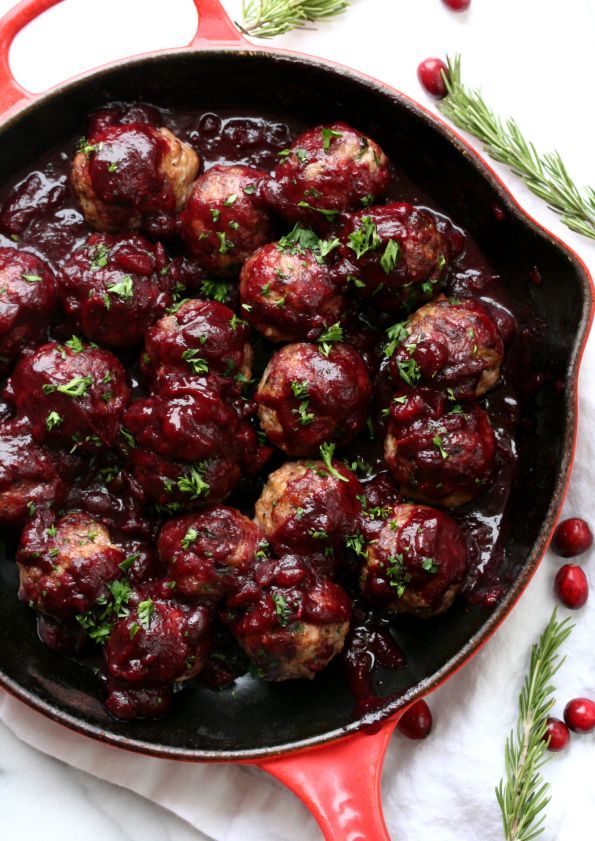 cranberry meatballs in a red skillet with fresh herbs on the side