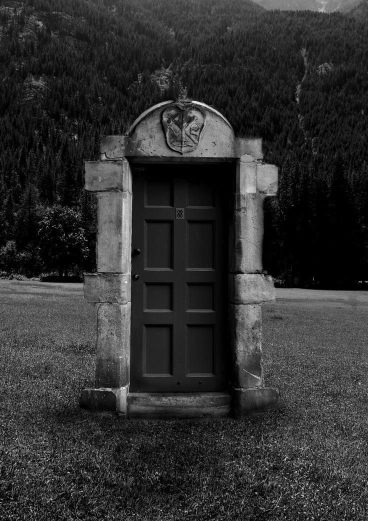 black and white photograph of an old door in the middle of a field with mountains in the background