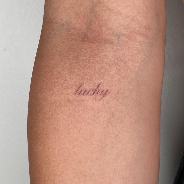 a woman's arm with the word lucky tattooed on her left side, in cursive font