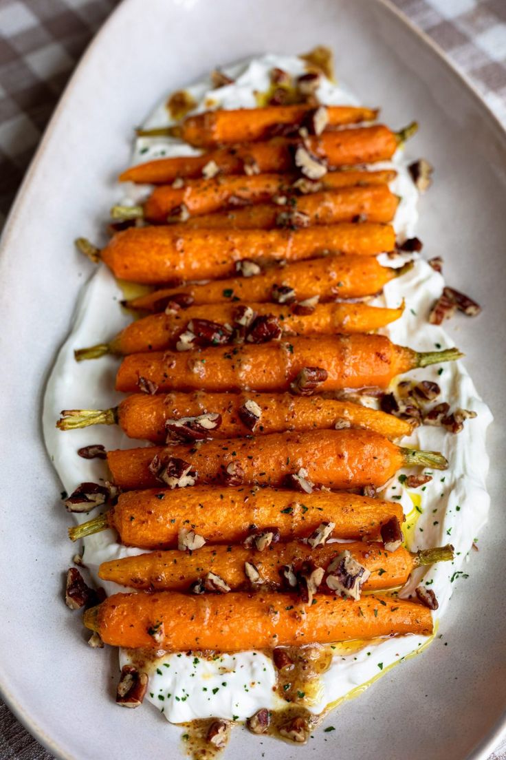 a white plate topped with carrots covered in whipped cream and chopped nuts on top