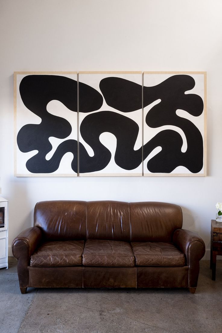 a brown leather couch sitting in front of two black and white paintings