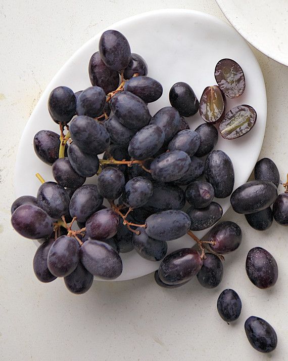 a white plate topped with black grapes next to an orange