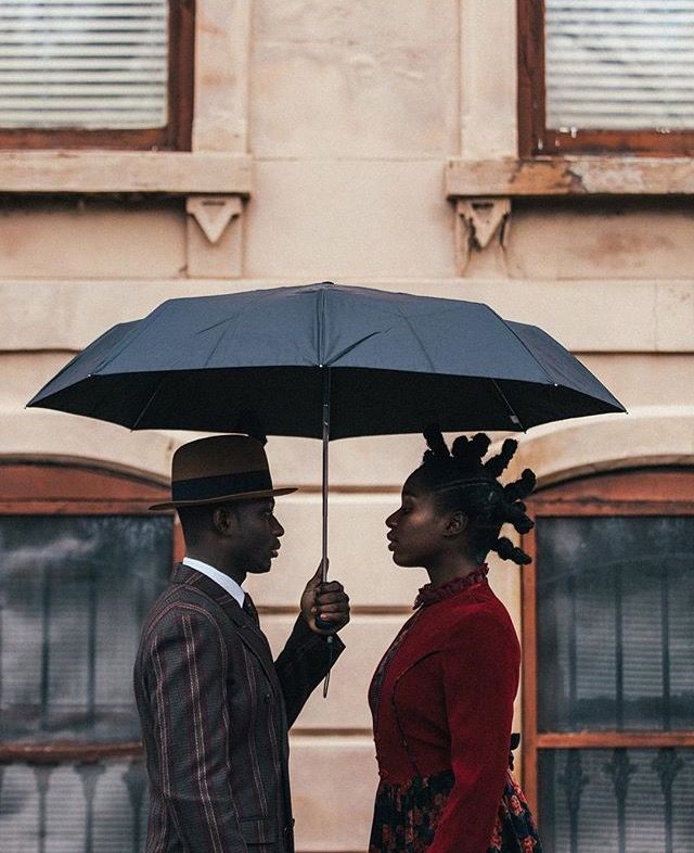 a man and woman standing under an umbrella in front of a building with two windows