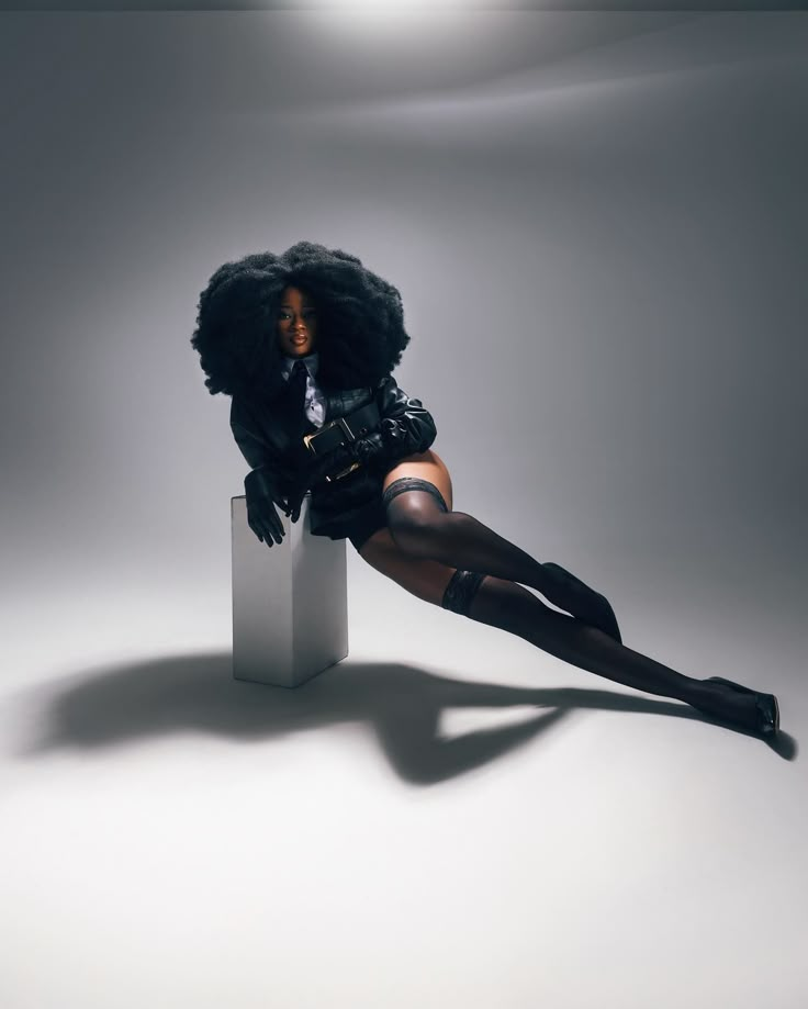 a woman is sitting on top of a white block with her legs crossed and wearing black stockings