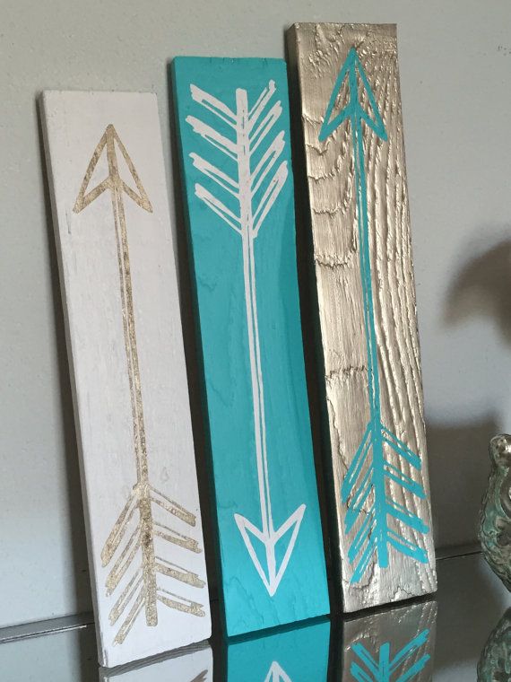 three wooden arrows painted in turquoise, white and gold on a shelf next to a vase