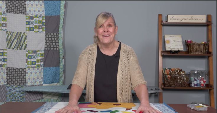 a woman sitting at a table in front of a quilt