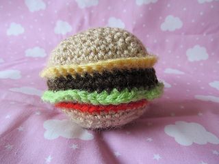 a crocheted hamburger sitting on top of a pink blanket