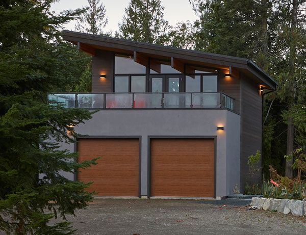 a two story house with wood garage doors and windows on the second floor, surrounded by trees