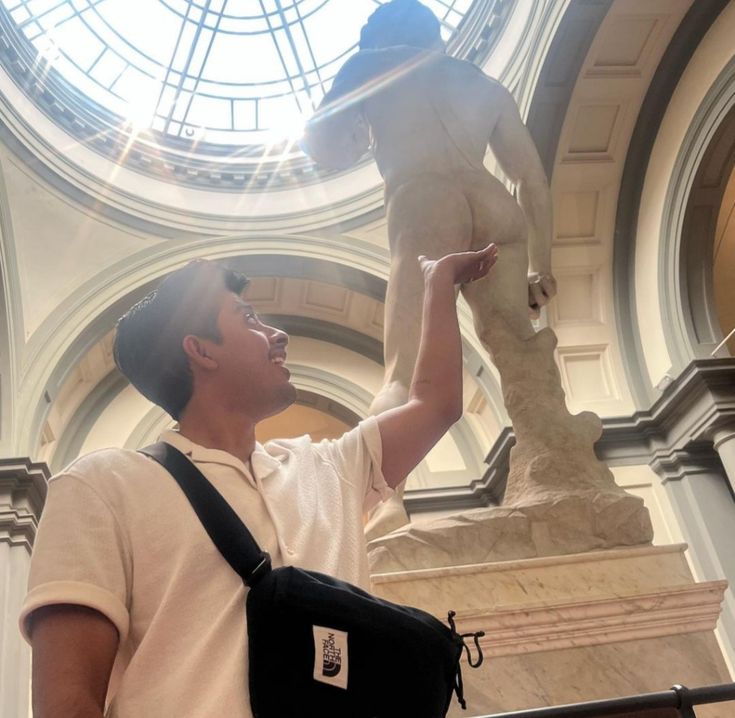 a man standing next to a statue in a building with a skylight above it