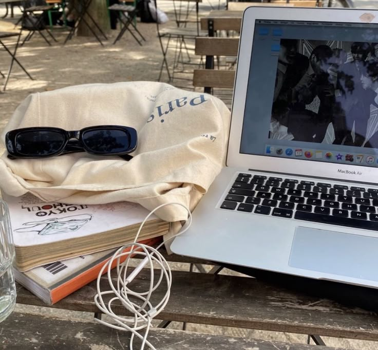 an open laptop computer sitting on top of a wooden table next to books and glasses