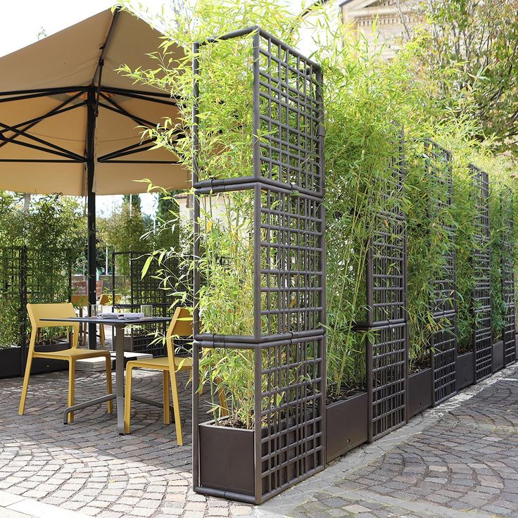 an outdoor dining area with tables, chairs and plants on the fenced in area