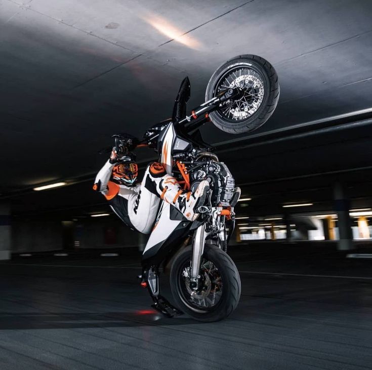 a person on a motorcycle doing a wheelie in an empty parking garage with dark lighting