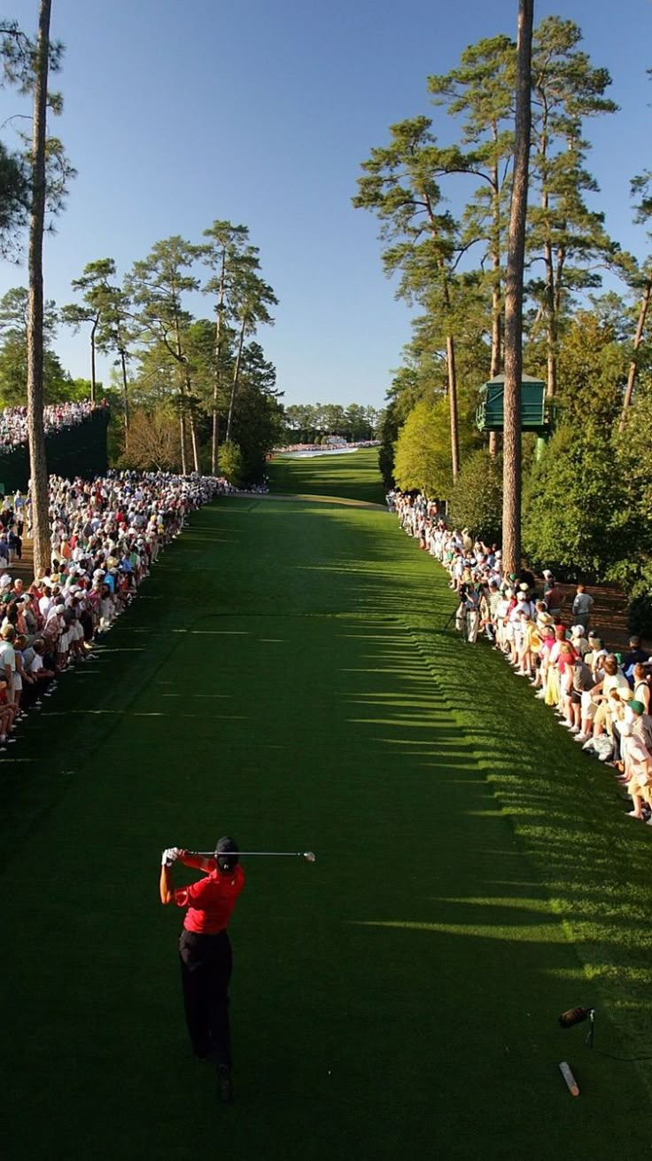 a man swinging a golf club on top of a lush green field with lots of people watching