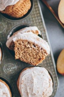 cupcakes with white frosting and apples on the side in a muffin tin